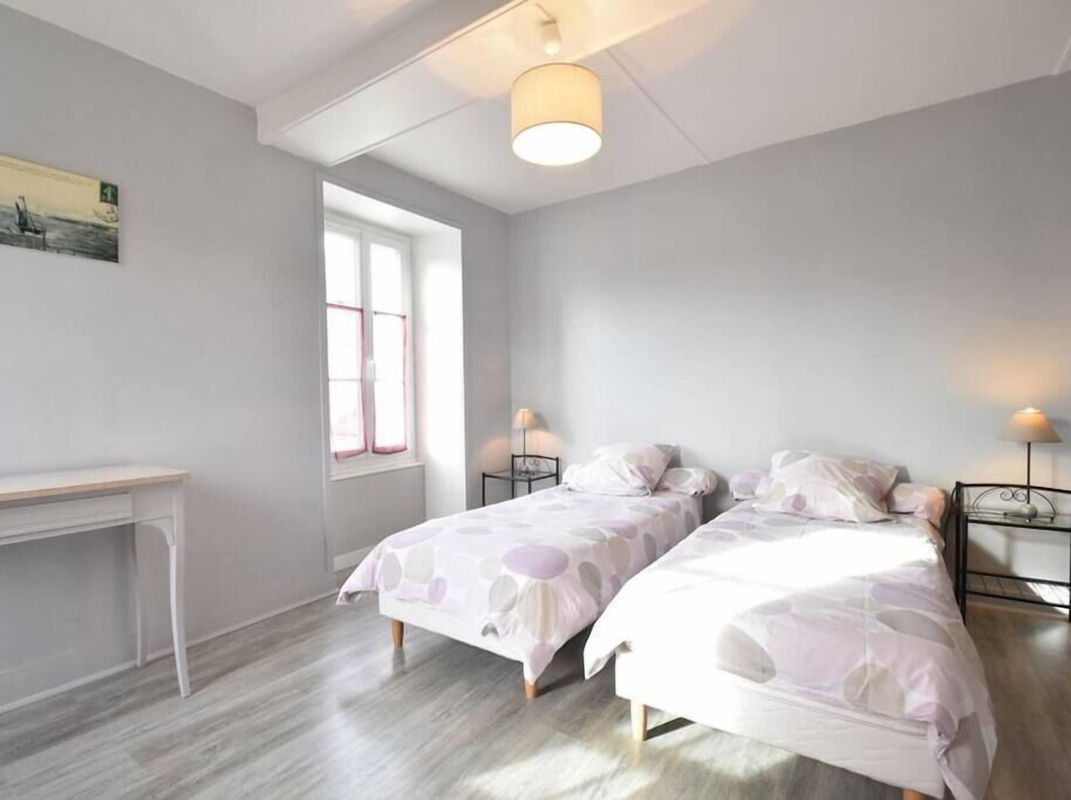 A bedroom with two beds, a desk, and a window.