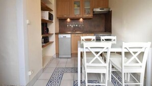 A compact kitchen with wooden cabinets, a dishwasher, and a dining area with white chairs.