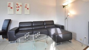 A modern living room with a black leather sectional sofa, a glass coffee table, and three wall-mounted paintings of red flowers.