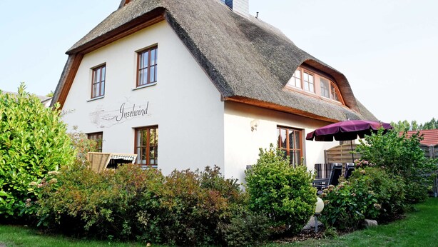 A traditional building with a thatched roof, a sign reading "Inschwind," and a patio area with outdoor seating.