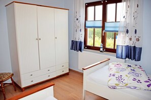 Een slaapkamer met een bed, een kledingkast, een raam met gordijnen en een radiator.