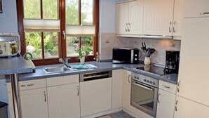 A kitchen with a dishwasher, oven, microwave, and a window with blinds.