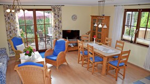 A cozy living room with wicker furniture, a dining table, and a TV.