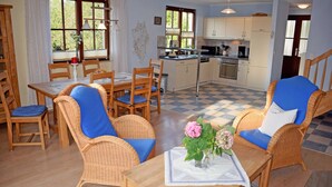 A cozy living area with wicker furniture, a dining table, and a kitchen in the background.