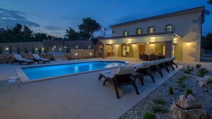 Una piscina con sillas de descanso, un muro de piedra e iluminación exterior en un edificio.