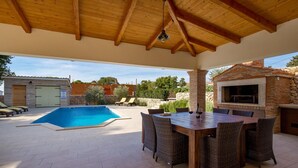 Un área de piscina al aire libre con un pérgola de madera, una parrilla y sillas de descanso.