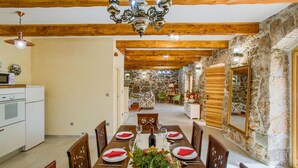 Un comedor con mesa de madera dispuesta para cuatro personas, una araña y paredes de piedra.