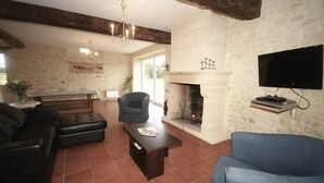Una sala de estar con chimenea, televisor montado en la pared, sofá, mesa de centro y una silla.