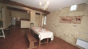Un comedor con una mesa larga dispuesta para cuatro personas, un banco de madera y una pared de piedra con un tapiz.