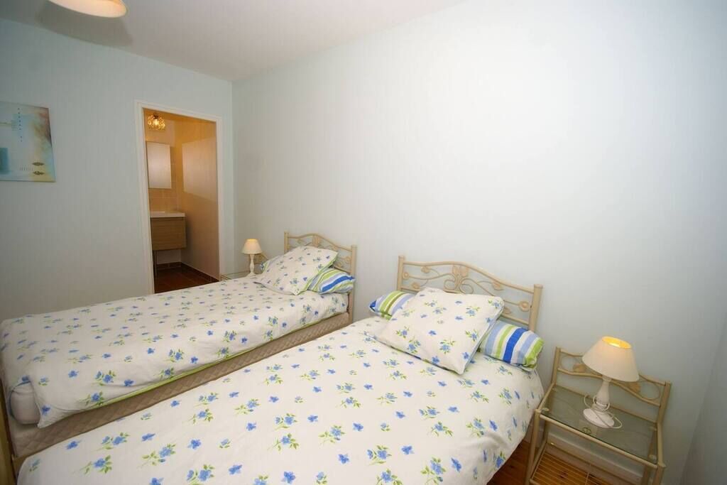 A room with two single beds, each with a wooden headboard and a bedside table with a lamp.
