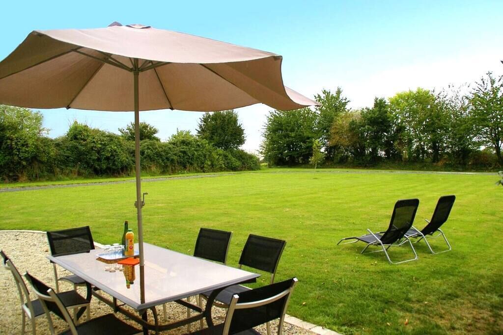 Un patio con una mesa, sillas, una sombrilla y un césped.