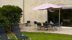 Un patio al aire libre con mesa y sillas, una parrilla y un paraguas grande.