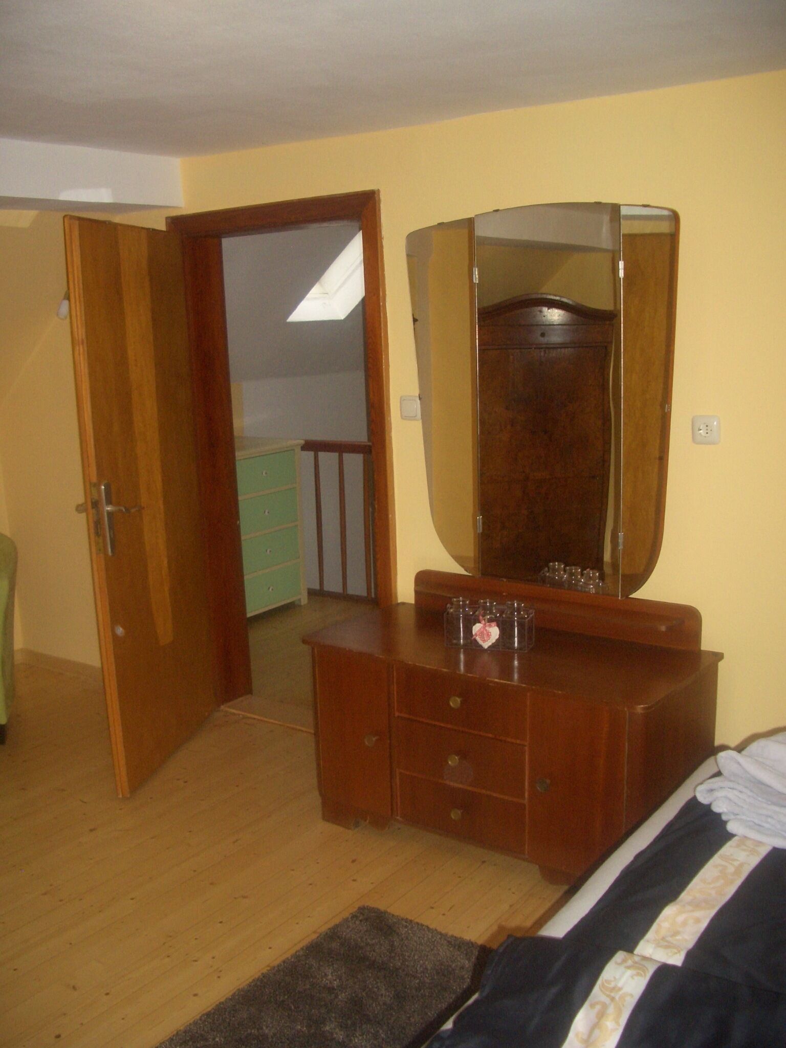 A bedroom with a wooden dresser, a large mirror, a bed with a patterned bedspread, and a small rug.