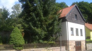 Una casa de dos pisos con tejado de tejas rojas, fachada de piedra y cerca de madera.