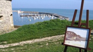 Une vue sur la côte, avec une tour en pierre, une zone herbeuse et un port de plaisance avec des bateaux.