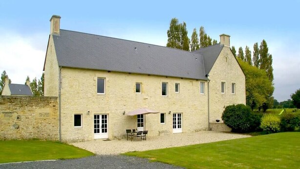 Un bâtiment en pierre de deux étages, avec une allée en gravier et un patio doté de meubles pour se détendre en plein air.