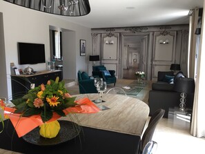 Un salon moderne comprenant un coin repas, un téléviseur fixé au mur et un lustre.