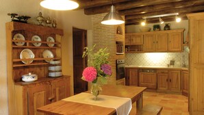 Een houten eettafel met een bloevas, een houten kast met servies en een bakstenen muur.