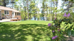 A house with a deck, a lawn, and a lake in the background. - Enjoy the lake, dock, beach, large grounds, or renovated home.  New ductless AC. (East Falmouth)