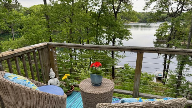 A wooden deck with wicker furniture, a Buddha statue, and potted plants. - Enjoy the lake, dock, beach, large grounds, or renovated home.  New ductless AC. (East Falmouth)