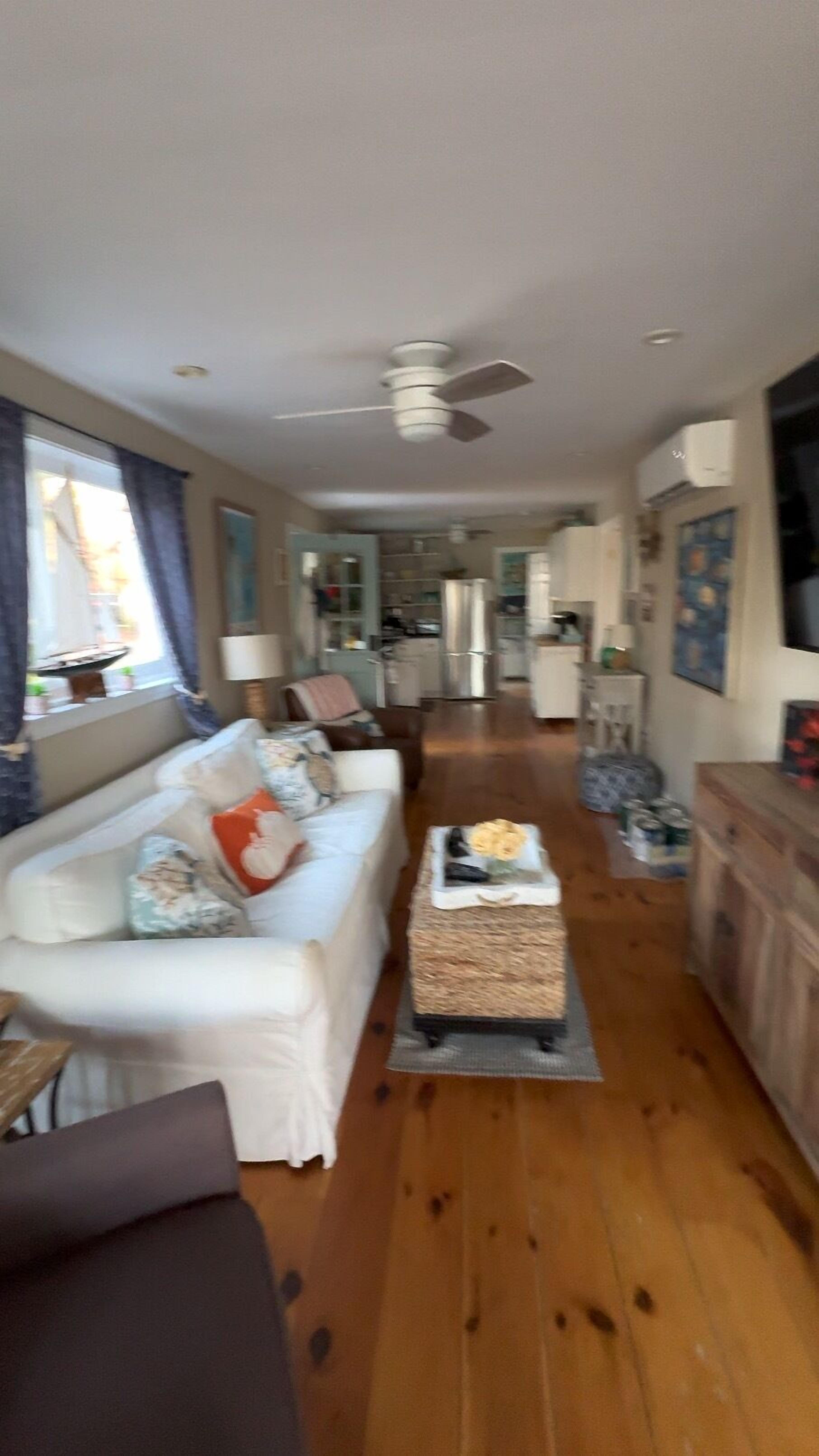 A living room with a sofa, a coffee table, and a television. There is a kitchen area in the background.