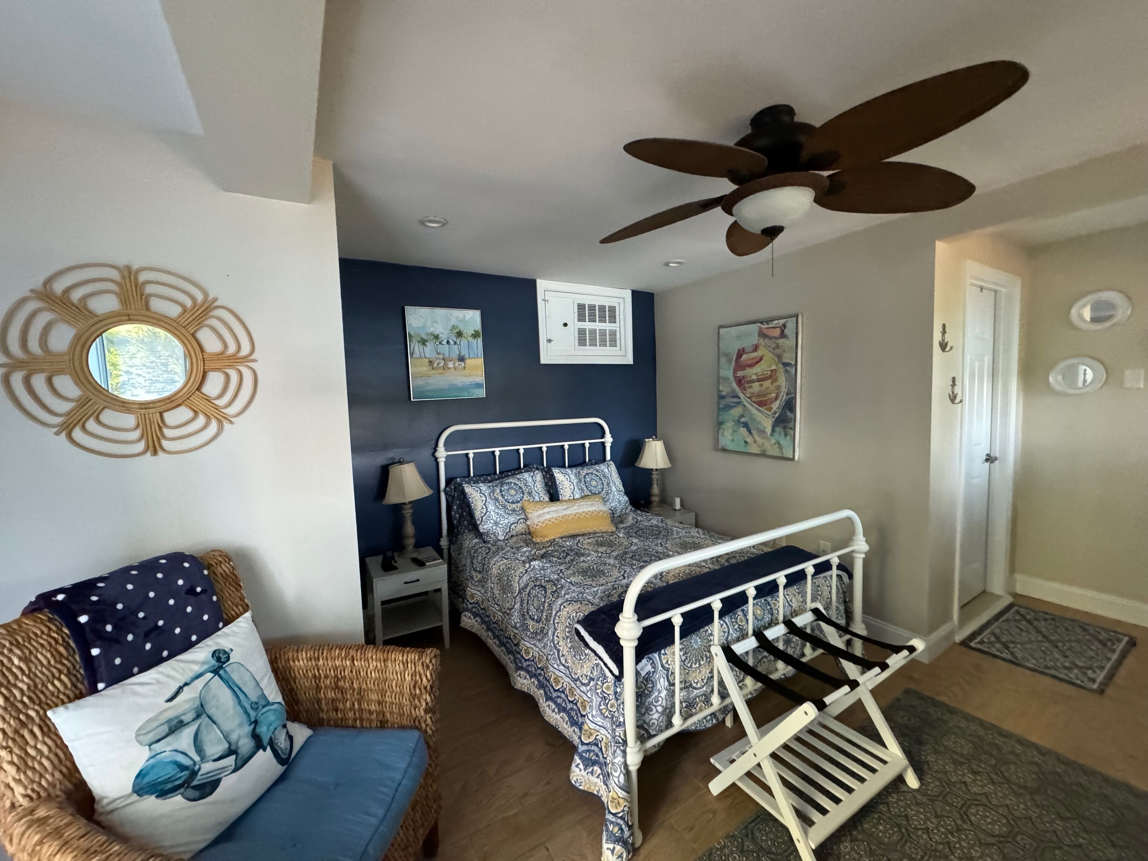 A bedroom with a bed, a chair, a ceiling fan, and artwork on the walls.