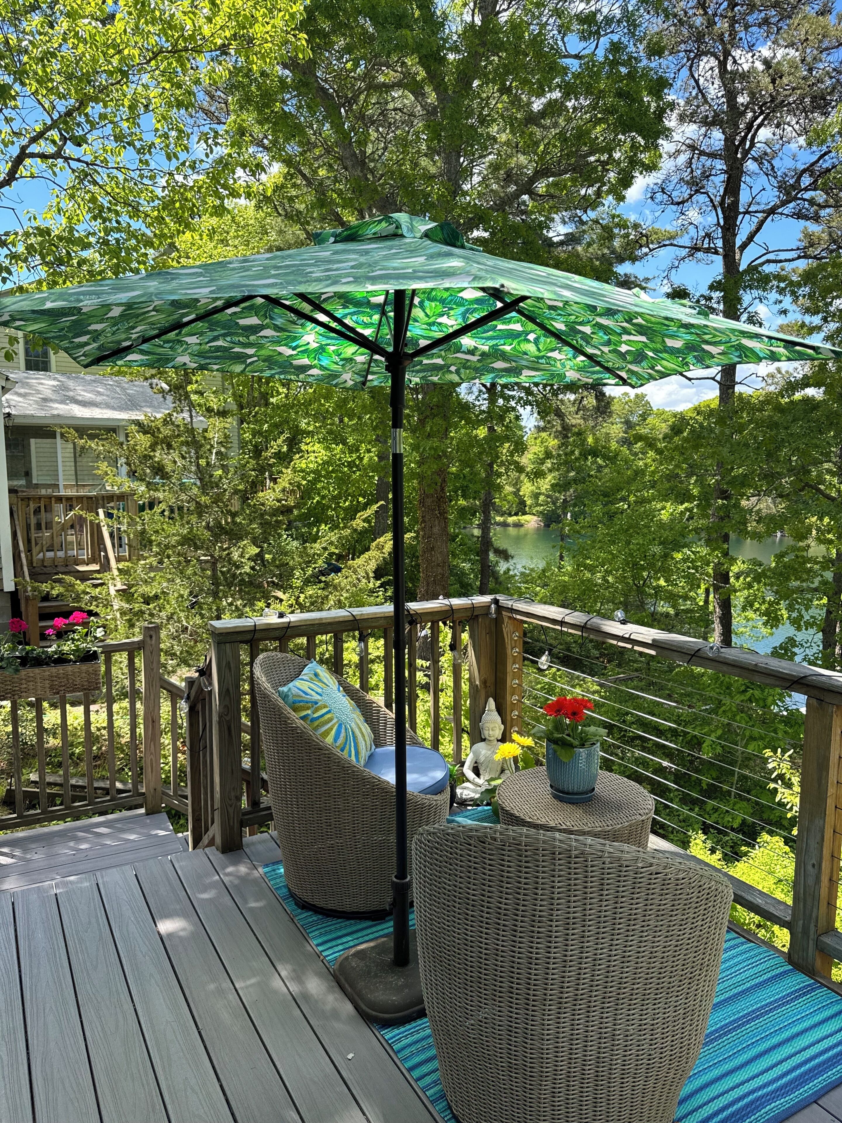 Een houten terras met rieten meubilair, een groene parasol en een Boeddhabeeld.