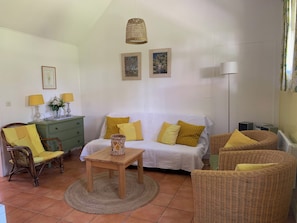 A living room with a sofa, two chairs, a table, a lamp, and a hanging light fixture. - Chalet with large fenced garden at the foot of the dunes, pets allowed (Mimizan)
