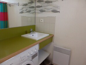 Une salle de bain avec un plan de toilette vert, un lavabo blanc, un miroir et un lave-linge.