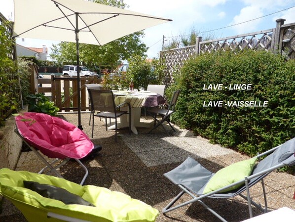 Un espace extérieur aménagé en terrasse, avec une table et des chaises, un grand parasol et une haie.