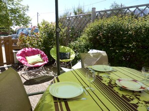 Un espace de restauration en plein air avec une table dressée pour deux personnes, entouré de verdure et délimité par une clôture en bois.