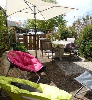 Un espace extérieur aménagé en terrasse, avec une table et des chaises, un grand parasol et une haie.