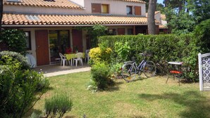 A two-story house with a tiled roof, a covered patio with outdoor seating, and a bicycle parked outside. - House 50 m2, terrace, enclosed garden, pine forest, private parking, shared swimming pool (Les Mathes)