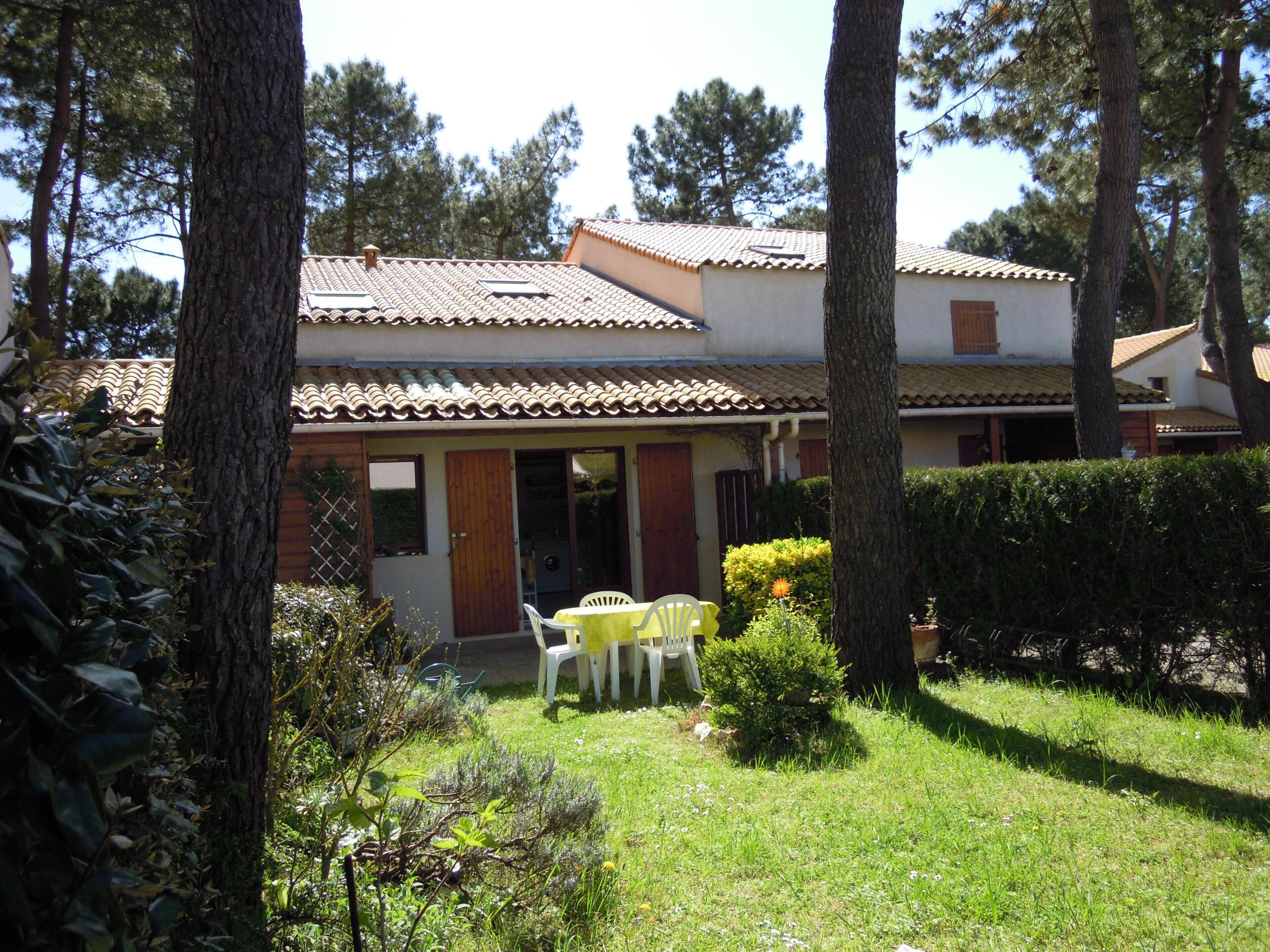 A two-story house with a tiled roof, a front door, and a small patio with a table and chairs.