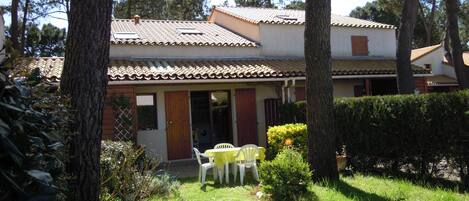 A two-story house with a tiled roof, a front door, and a small patio with a table and chairs.