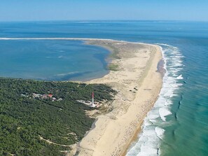 Vue aérienne d’une zone côtière comprenant une plage, un phare et une zone boisée.