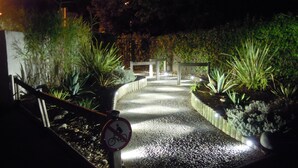 A nighttime garden pathway with a no bicycle sign, surrounded by various plants and illuminated by ground lights. - House 50 m2, terrace, enclosed garden, pine forest, private parking, shared swimming pool (Les Mathes)