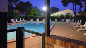 A swimming pool with lounge chairs, surrounded by trees and a building in the background. - House 50 m2, terrace, enclosed garden, pine forest, private parking, shared swimming pool (Les Mathes)