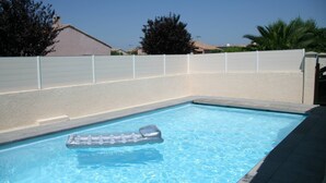 Una piscina rettangolare con acqua cristallina blu, circondata da una recinzione bianca e un muro color beige.