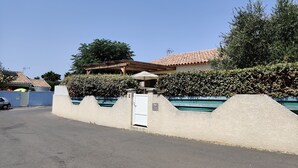 Un'area residenziale recintata con piscina, un gazebo e una casa con tetto in tegole.