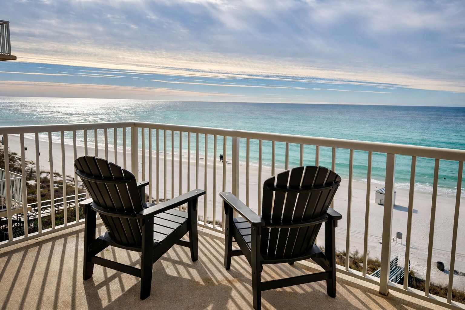 A balcony with two Adirondack chairs overlooking a beach with a clear view of the ocean.
