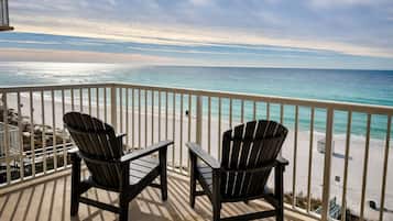 A balcony with two Adirondack chairs overlooking a beach with a clear view of the ocean.