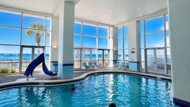 An indoor swimming pool with clear views of the ocean through large windows, a slide, and lounge chairs. - Steps to the Sand at our Beachfront Condo at Majestic, 5th floor convenience  (Panama City Beach)
