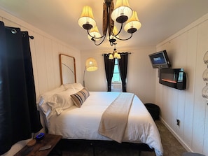 A bedroom with a bed, a television mounted on the wall, a ceiling light fixture, and a window with curtains. - 5 ★ FISH HOUSE Sleep on the Pond and see Scottish Highland cows while fishing (New Market)