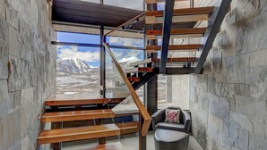 Ein modernes Interieur mit einer Wendeltreppe, Steinwänden und Blick auf schneebedeckte Berge.