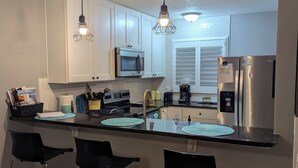A modern kitchen with white cabinets, stainless steel appliances, and black bar stools. - Steps to the beach and restaurants!!! (St. Augustine)