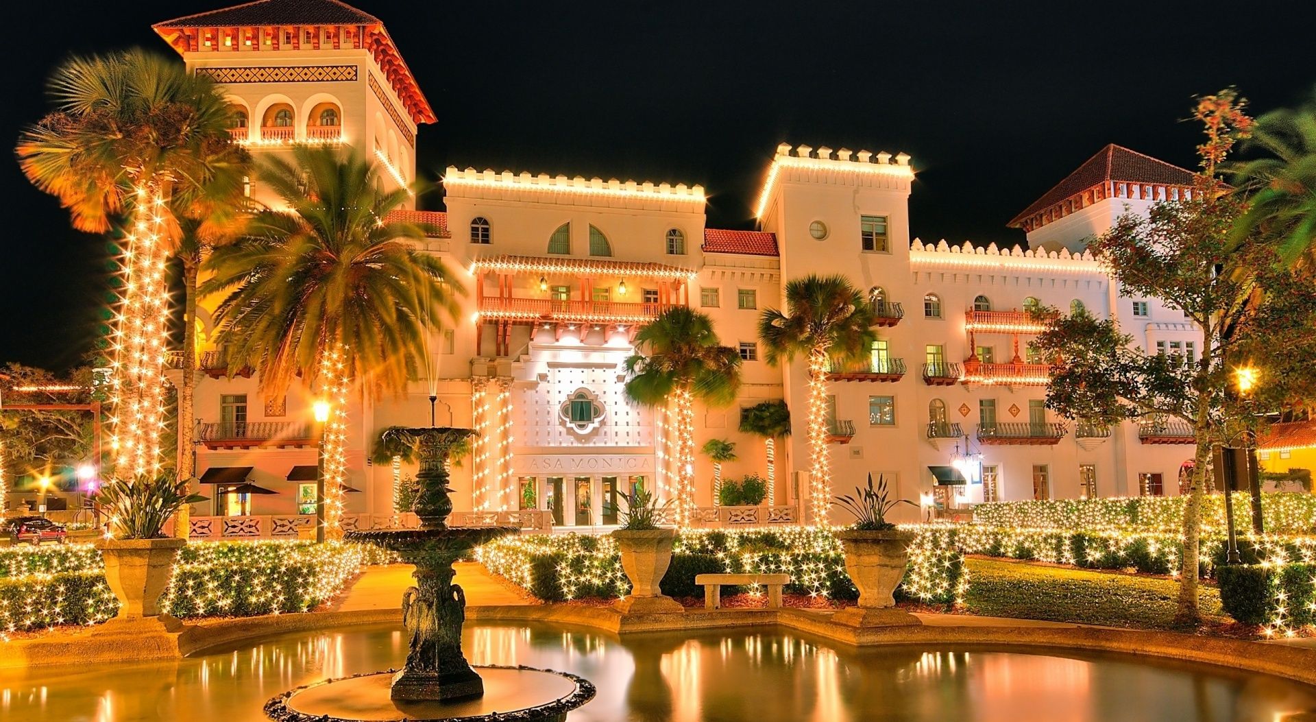 A hotel with a fountain, palm trees, and string lights.