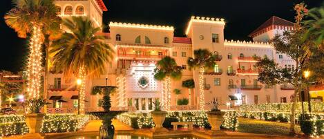 A hotel with a fountain, palm trees, and string lights.