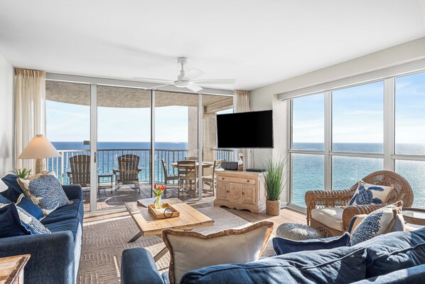 Ein geräumiges Wohnzimmer mit großem Fernseher, bequemen Sitzgelegenheiten, einem Balkon mit Meerblick und einem Deckenventilator.