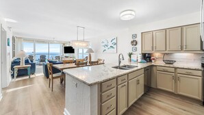 A spacious kitchen with a large island, a dining area with a view, and a living room with a sofa and chairs. - Spectacular Views-Gulf Front Corner unit - Hidden Dunes Gulfside 1506 (Miramar Beach)